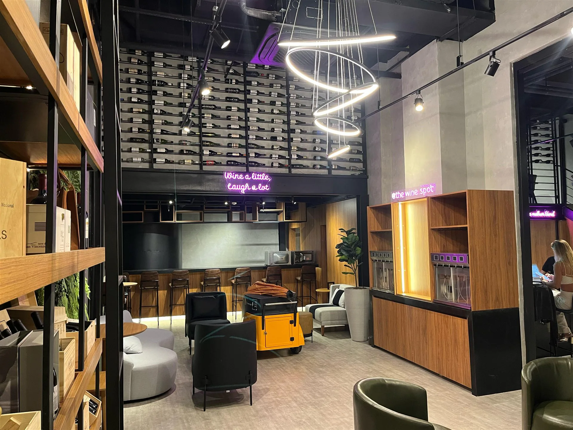 Lounge do The Wine Spot com iluminação moderna e garrafas ao fundo